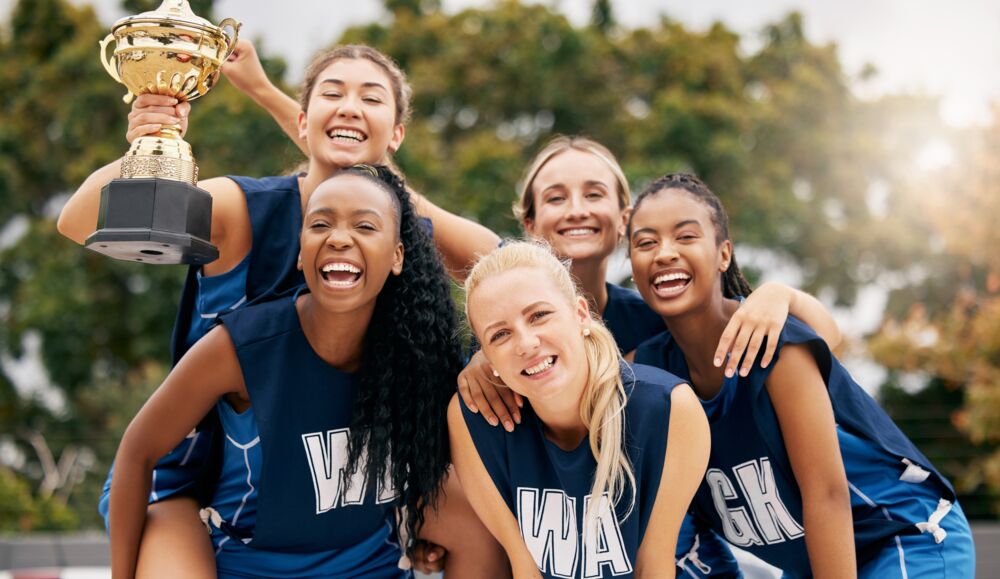 Netball team in matching club dresses celebrating with a trophy